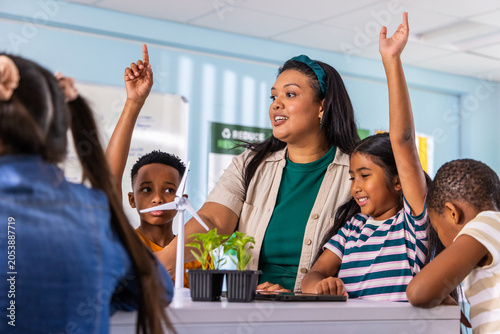 Diverse elementary students with female teacher doing STEM in class with wind turbine plants tablet