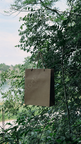 Eco-friendly craft paper bag mockup hanging outdoors in nature with a lake background