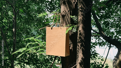 Empty brown paper shopping bag hanging on a tree in the forest
