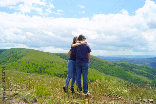 Foto Couple embraces on grassy mountain summit overlooking vast landscapes during hiking