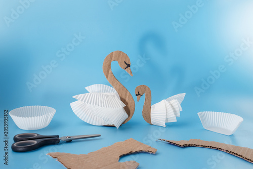 Fotografía Cardboard swan and cygnet craft made from corrugated paper and white cupcake liners on blue background
