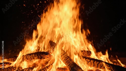 A bright campfire burns with intense orange flames at night