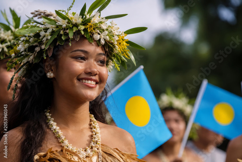 Portrait of woman wearing a floral headpiece, celebrating Constitution Day in Palau with flags.