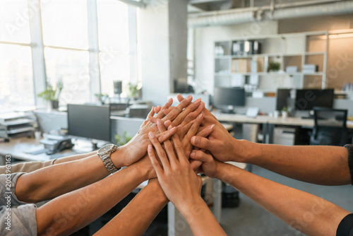 Group of diverse colleagues stacking hands together in modern office workspace