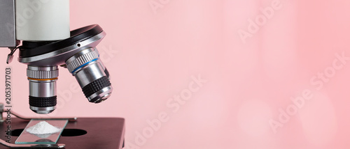 Close-up of a microscope objective focused on a pile of white powder on a glass slide against a pink background.
