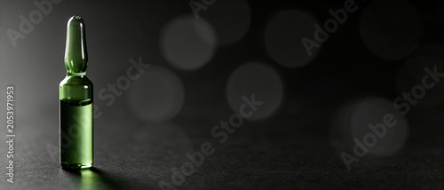 Close-up shot of a glass ampoule with green liquid on a dark background with soft blurry bokeh, representing a pharmaceutical concept.