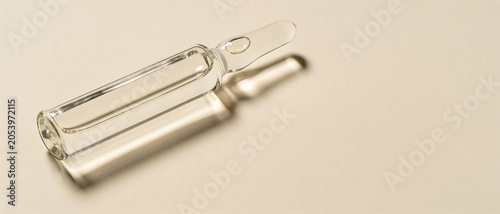 Transparent glass ampoule with medicinal liquid on a light beige background with a soft shadow.
