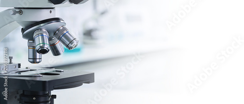 Close-up shot of a modern laboratory microscope with metallic lenses on a blurred bright laboratory background.