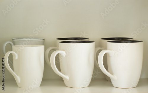 White ceramic mugs neatly arranged on a kitchen cupboard shelf, showing everyday household kitchenware.