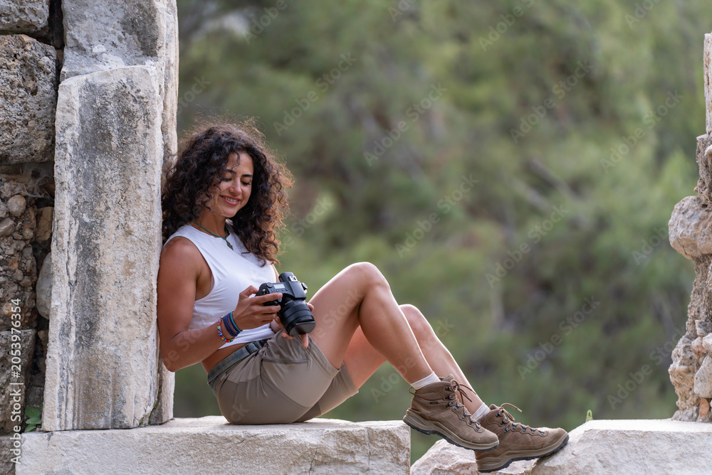 Fototapeta premium Young female photographer resting on ancient stone ruins at Phaselis, Turkey.