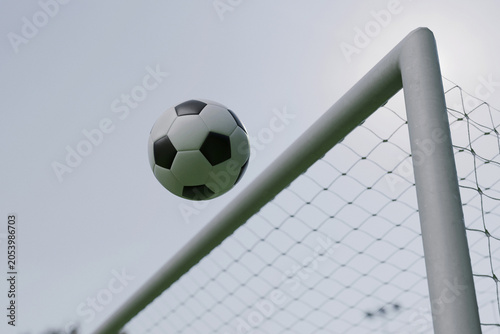 Classic soccer ball hitting the top corner of a football goalpost against a bright sky. Perfect shot capturing a dramatic scoring moment, victory, or successful striking during a match