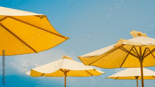 Fotografía Yellow patio umbrellas against a soft, bright blue sky.
