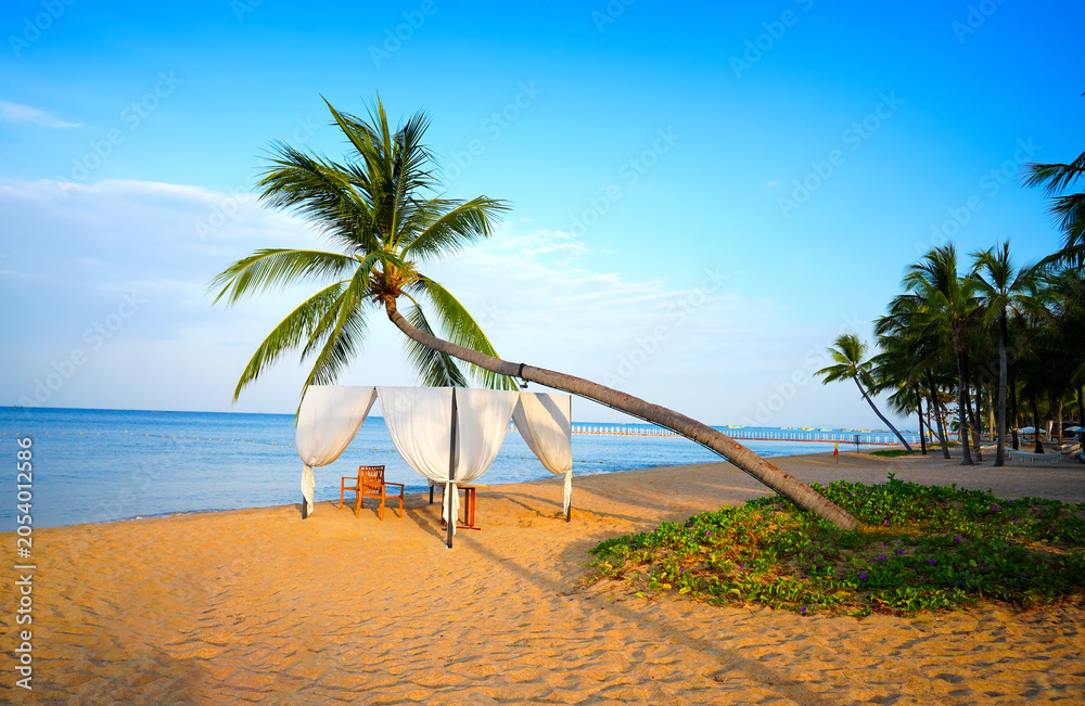 Obraz premium Beach setting with tent and palm trees. Beneath palm tree, secluded beach cabana with white curtains and chairs offers relaxation for guests. Picturesque Long Beach on ​​Phu Quoc Island in Vietnam