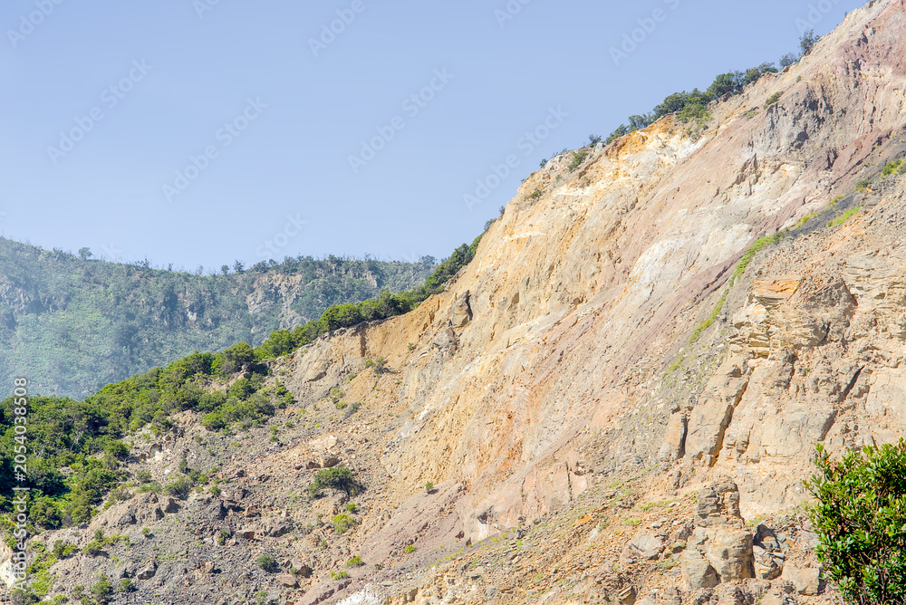 Fototapeta premium Dramatic landscape view of a steep, eroded mountain slope with exposed rocky cliffs and sparse vegetation under a clear blue sky in a rugged natural environment