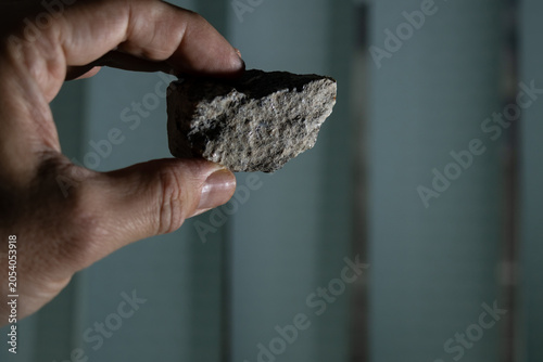 Holding a dark stone in hand; vertical window blinds in the background