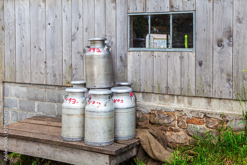 Milk cans stacked beside a wooden building in a rural setting