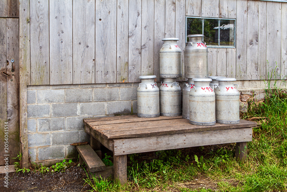 Obraz premium Milk Milk cans stacked beside a wooden building in a rural setting
