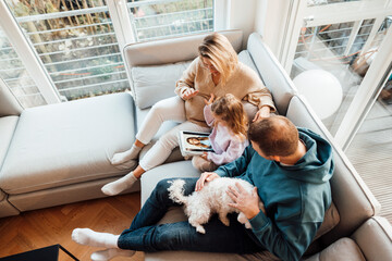 Daughter looking at photos with parents and dog sitting on sofa at home