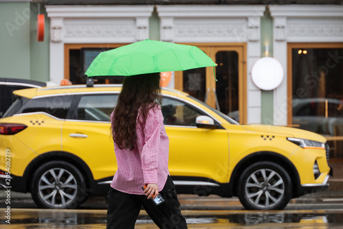 Girl with umbrella walking on city street on taxi car background, rainy weather