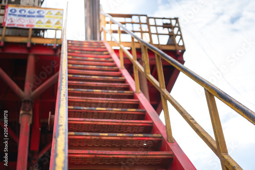 Fotografie A low-angle perspective shot of industrial red steel stairs leading up to Rig floor of onshore oil drilling rig under a bright sky