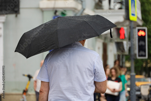 Man with umbrella standing on city street on red traffic light background, rainy weather