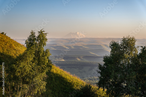 Bild auf Leinwand Panoramic view of the green valley and the snowy peak of Mount Elbrus on the hor