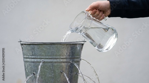 Wasted Effort Concept, Hand Pouring Water Into Leaky Metal Bucket