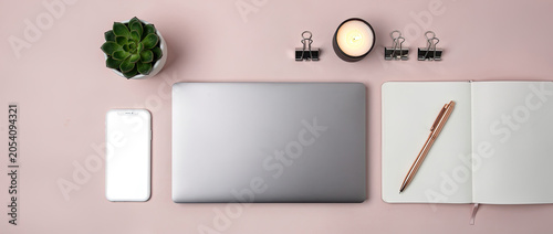 Flat lay of a modern workspace with a laptop, smartphone, notebook, pen, and succulent plant on a pink background.