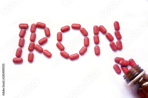 From the glass jar Iron supplement pills come out into the white background, Iron is used to treat anemia due to iron deficiency anemia. Iron written of red tablets.