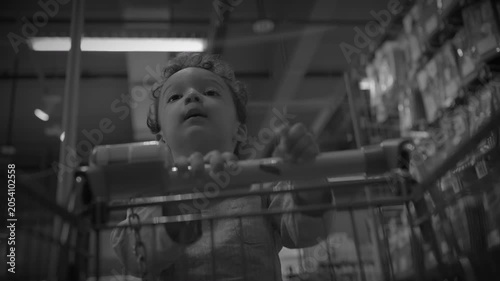 Curious child standing in shopping cart in supermarket aisle