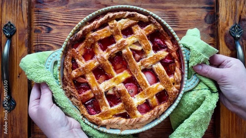 Woman placing homemade strawberry rhubarb pie on wooden table top view fresh baked dessert rustic pastry baking concept