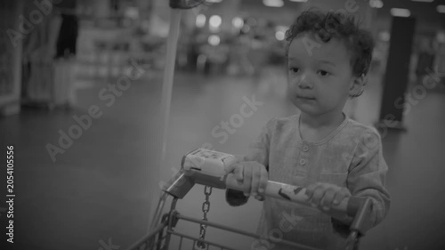 Young child pushing small shopping cart down store aisle in black and white