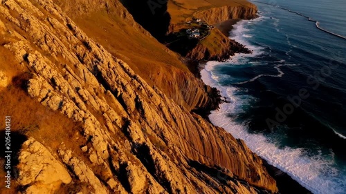 Aerial view of steep golden cliffs meeting the blue ocean waves at sunset