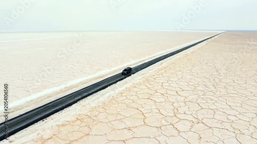 A single car driving on a long straight road through a vast dry salt flat landscape