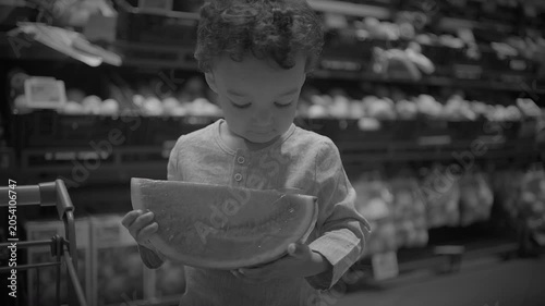 Child inspecting packaged lettuce in supermarket produce aisle, monochrome