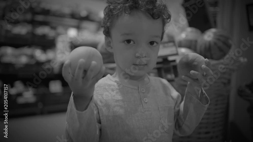 Toddler Standing in Supermarket Produce Aisle Holding Two Fruits