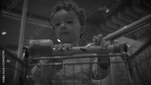 Toddler Boy Standing in Shopping Cart in Supermarket Aisle