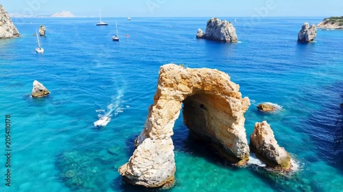 Natural stone arch in the blue ocean with boats sailing on clear water on a sunny summer day