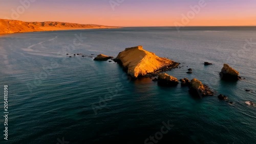 Small rocky island in the middle of a calm blue ocean at sunset with golden light
