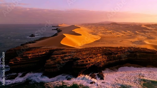Aerial view of golden desert sand dunes meeting the blue ocean waves at sunset