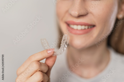 A woman holding clear aligners. Treatment for overbite, crowded teeth, and bruxism.