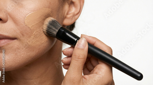 woman hands smearing foundation on face skin with make up brush with copy space on white background 