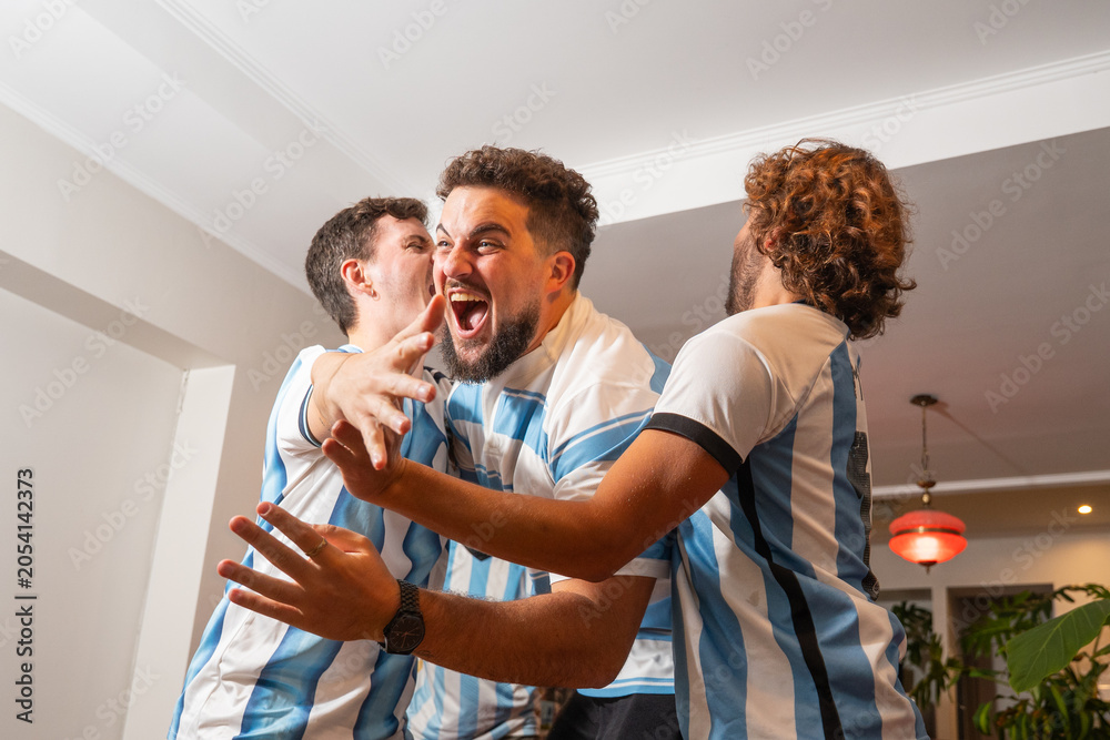 Obraz premium Grupo de amigos argentinos celebrando un gol mientras ven un partido de fútbol