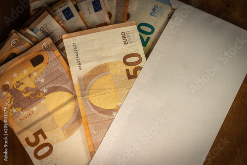 Photographie montrant une enveloppe blanche remplie de billets en euros. Notions de paiement, rémunération, prime, budget, dépenses, économies ou transaction financière en espèces