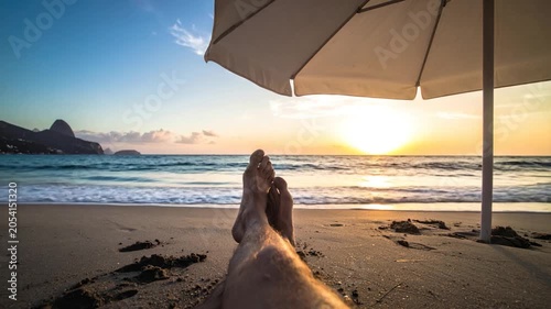 View from beach lounger of feet, waves, sunset and umbrella