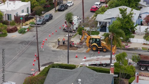 Construction workers repairing residential street with backhoe and traffic cones in San Diego, California. Overhead point of interest of urban infrastructure project