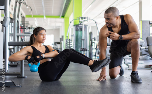 Konstfotografi Young woman performing a kettlebell core exercise while personal trainer at gym