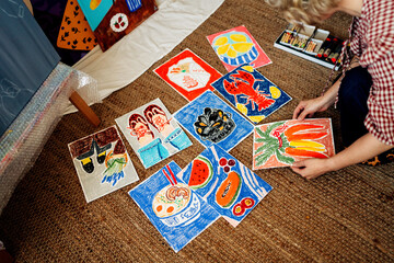 Artist arranging colorful drawings on floor in creative workspac