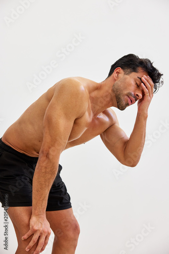 Man holds head with hand while standing against a plain wall