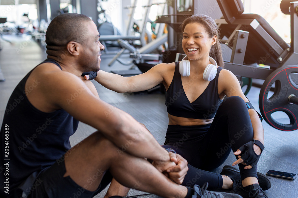 Naklejka premium Young black relaxing and talking after a workout in a modern gym. Fitness recovery, healthy lifestyle, social connection, and wellness concept
